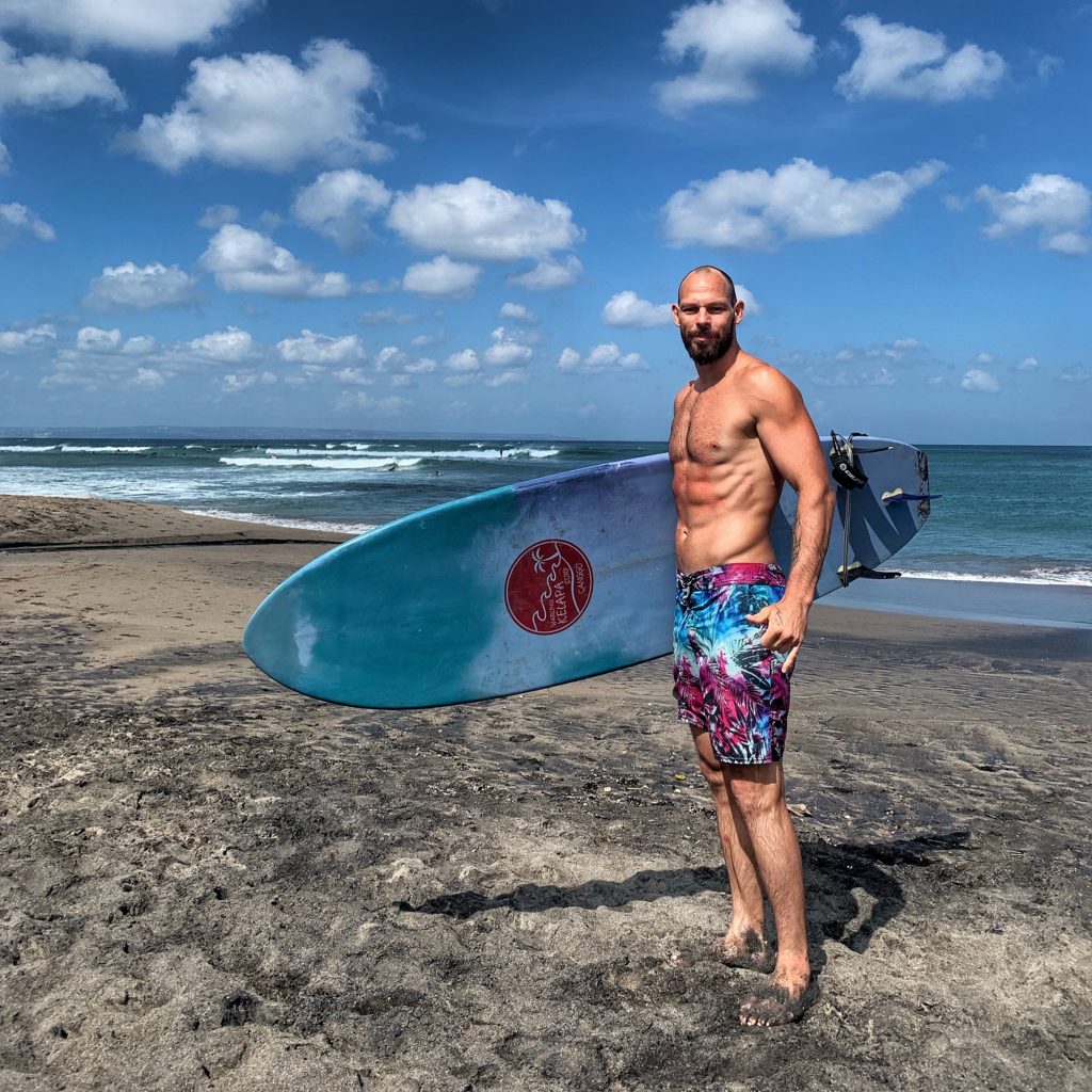 Doug Robson, stunt performer and yoga teacher, with a surfboard on a beach.