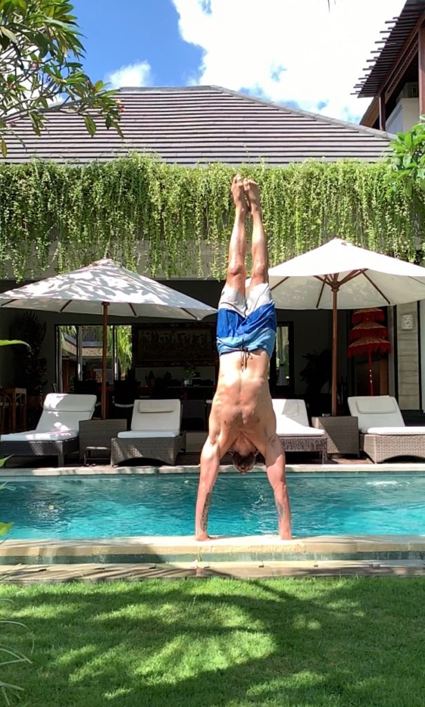Doug Robson doing handstand yoga in front of a pool.